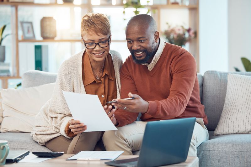 Couple in their 40s sitting on their couch and looking together at mortgage documents and a laptop