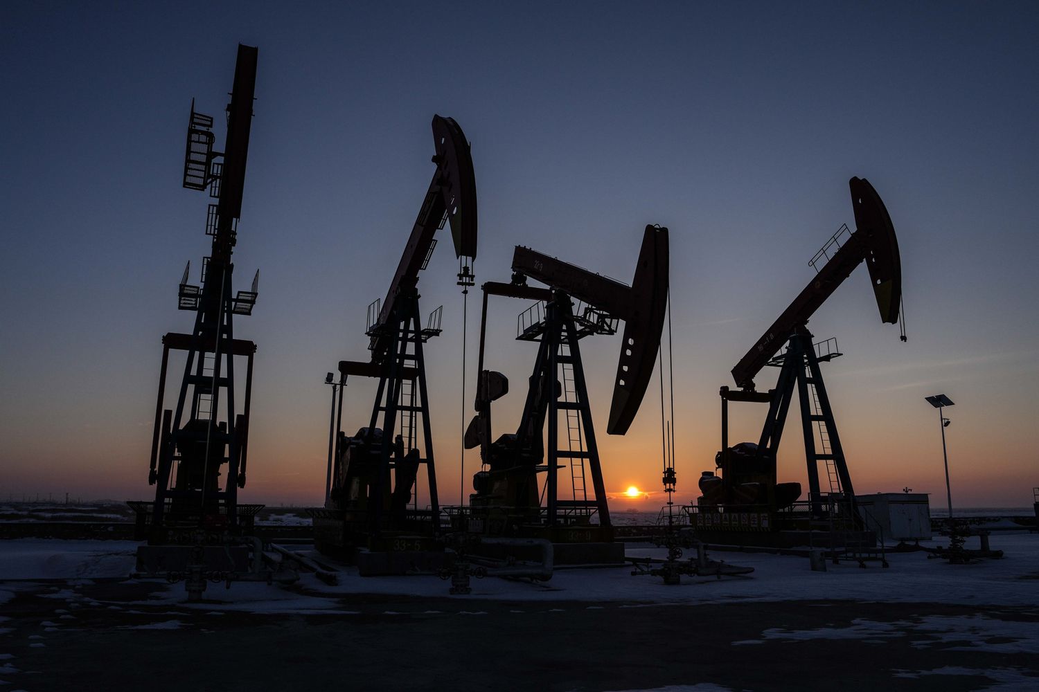 Silhouettes of oil derricks as sun rises in background. 
