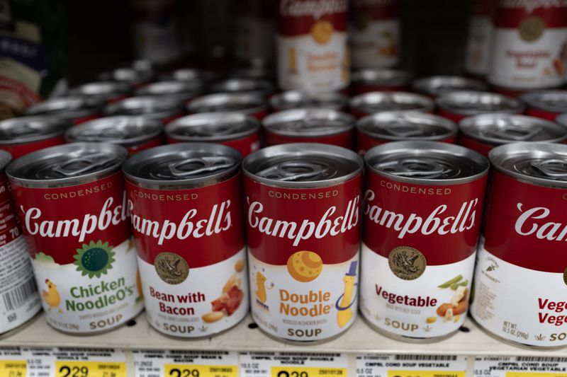 Rows of red and white Campbell's soup cans are seen on a shelf in a grocery store.