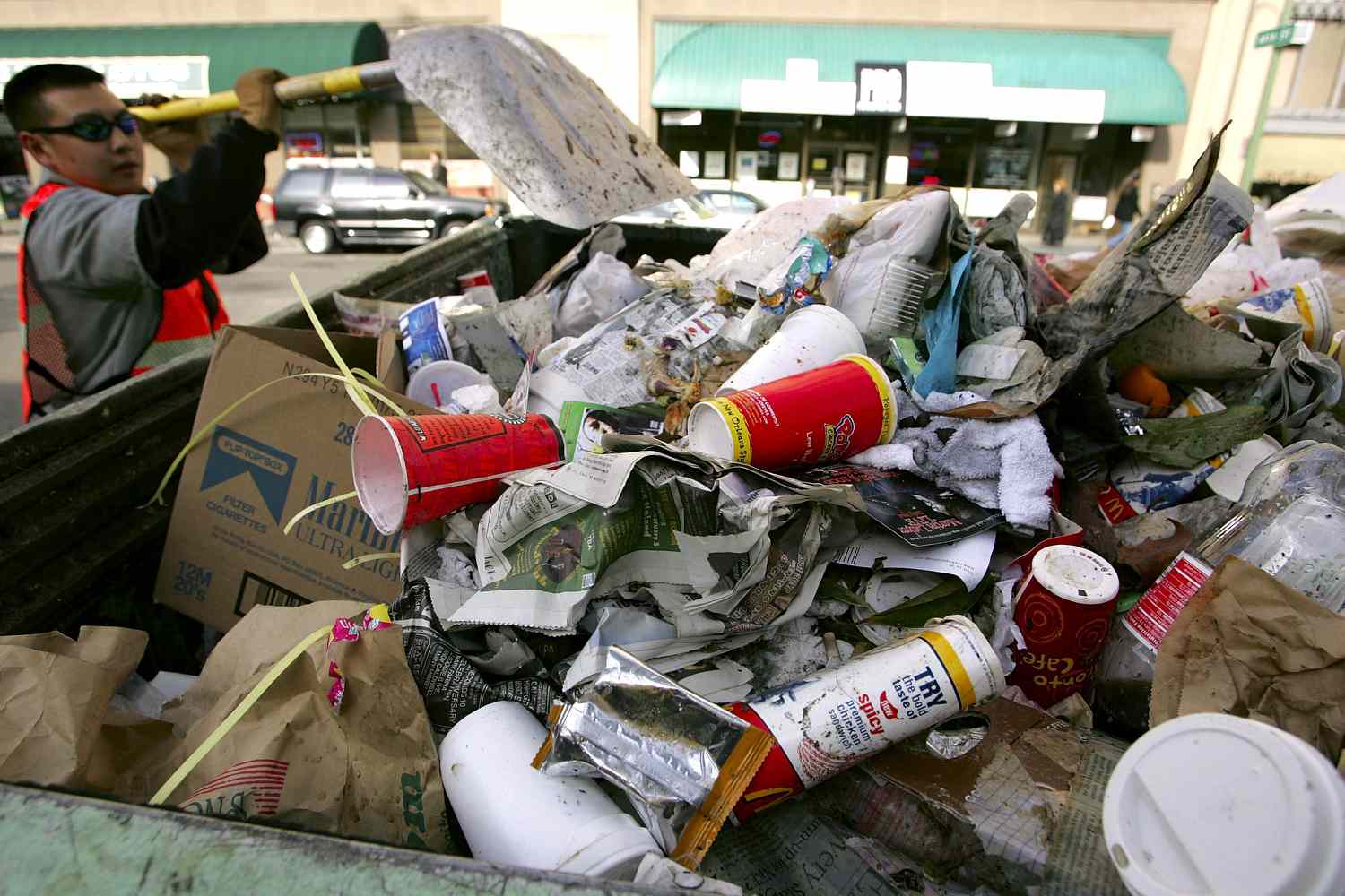 A street cleaning worker dumps trash, including branded fast food takeout cups, into a pickup truck