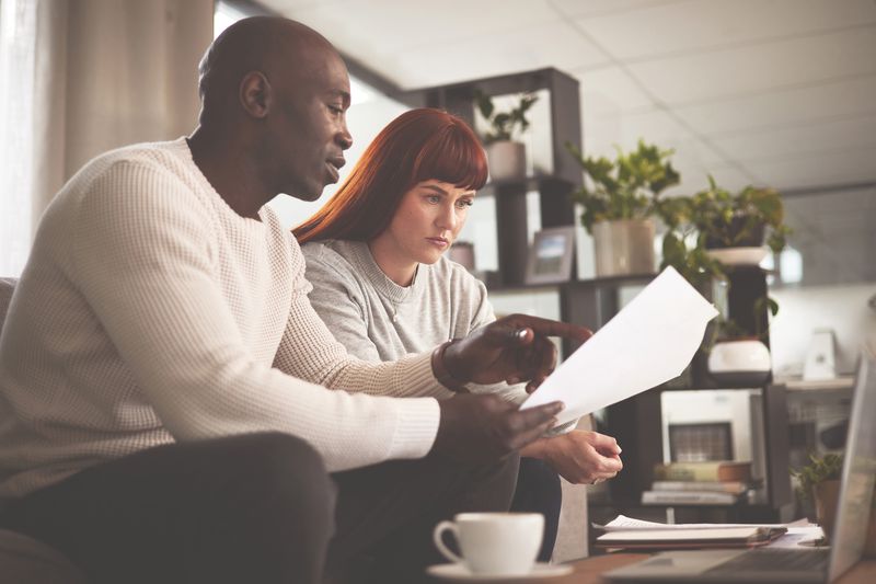 Couple in their 30s sitting on their sofa and looking at financial documents and online bank rates