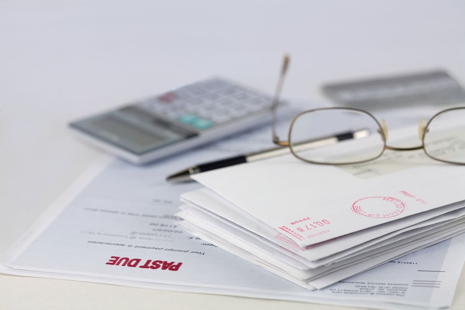 Stack of envelopes with pen, calculator, glasses and credit card.