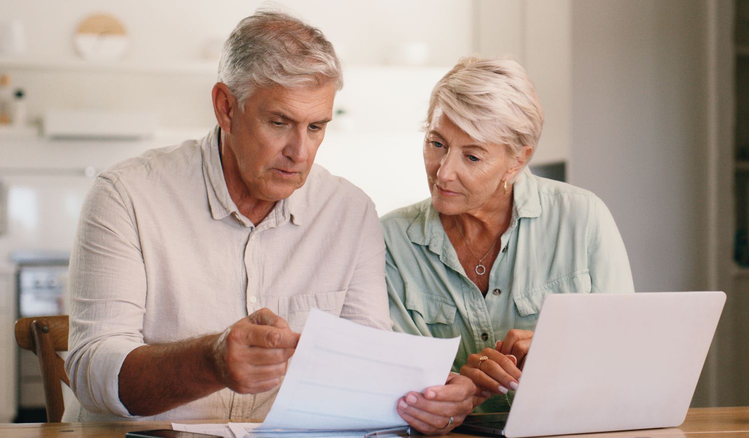 Older couple sitting at home and looking together at mortgage documents and a laptop
