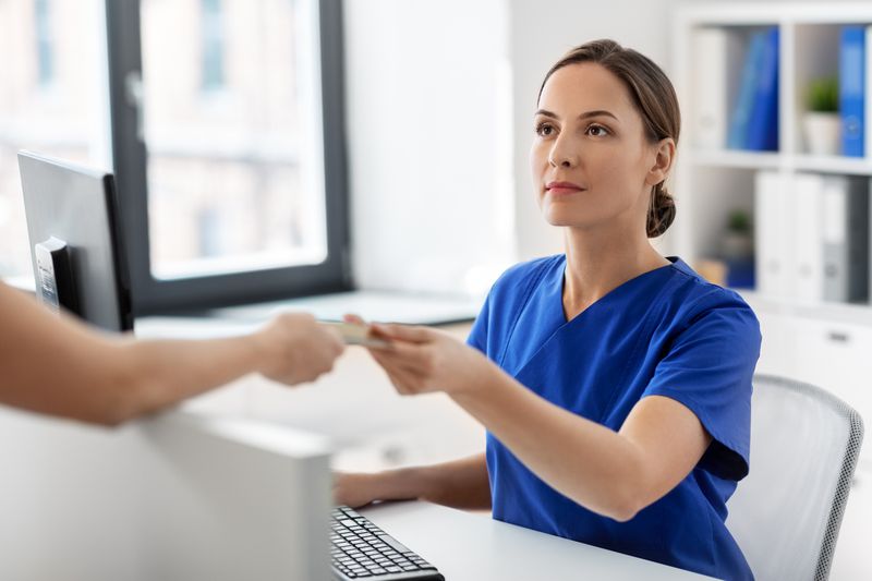 Woman in scrubs accepting payment card at medical desk