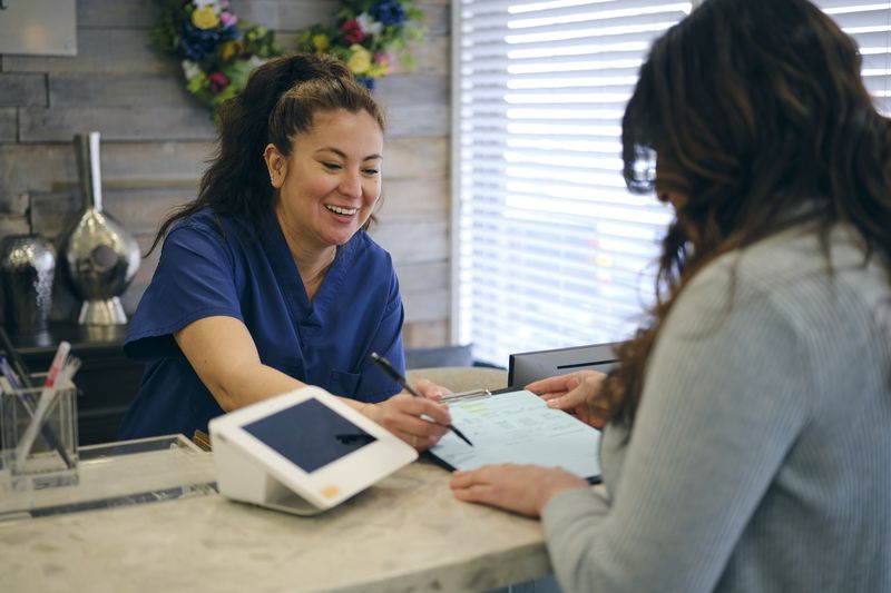 Woman at the front desk in a doctor's office showing paperwork to a patient