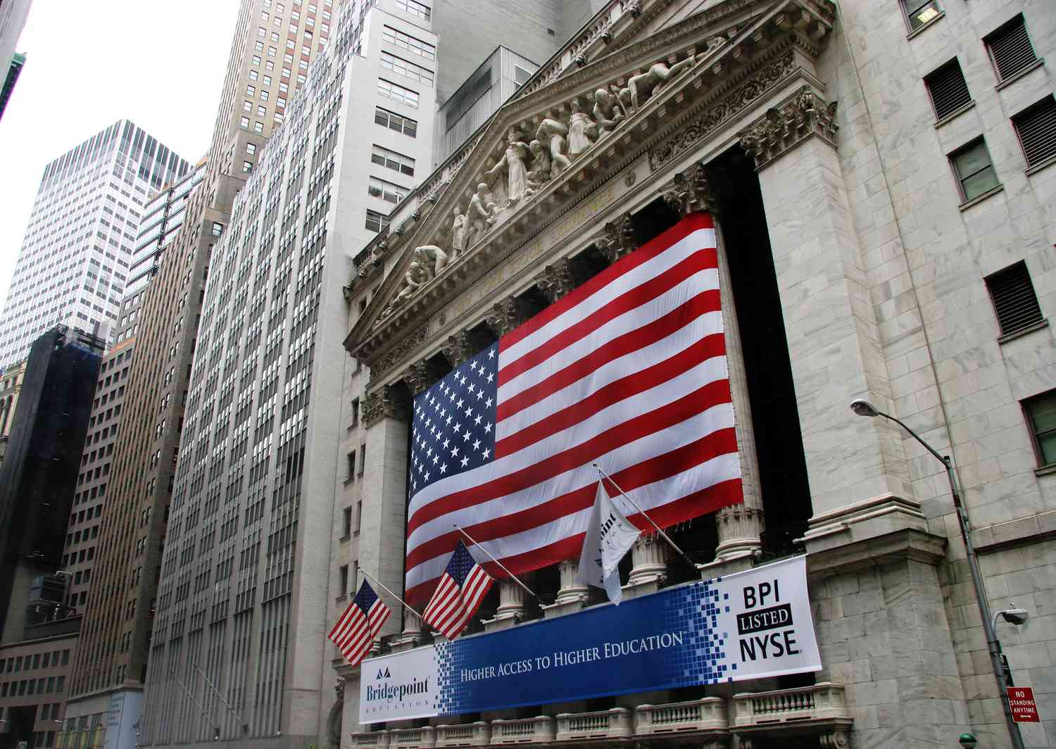 The exterior of the New York Stock Exchange on Wall Street, with a large American flag hanging from the facade.