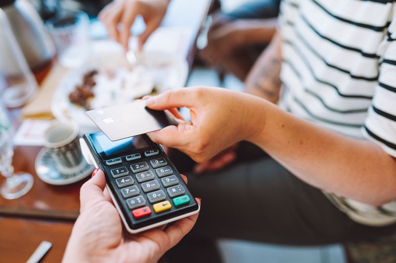 Person tapping their credit card against a card reader while sitting at a restaurant table