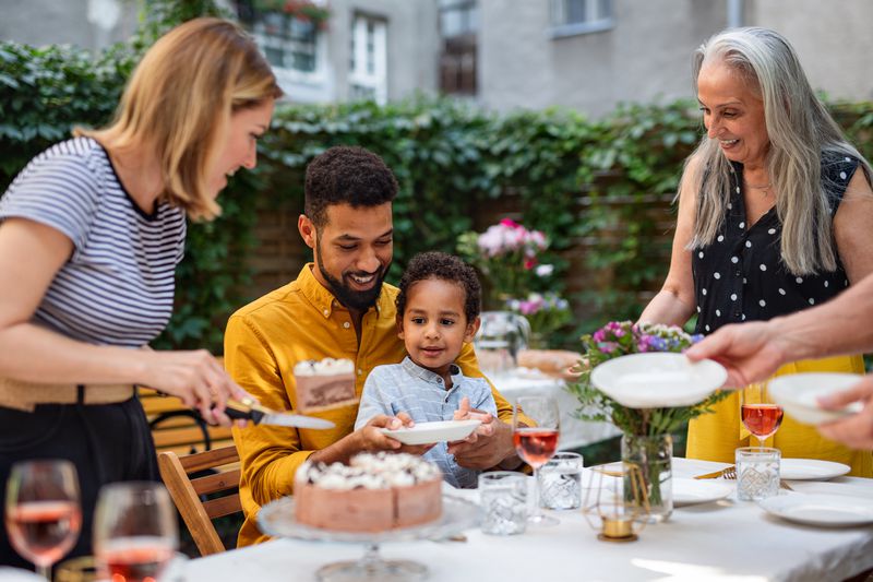 Happy multigeneration family having cake outdoors in garden at home.