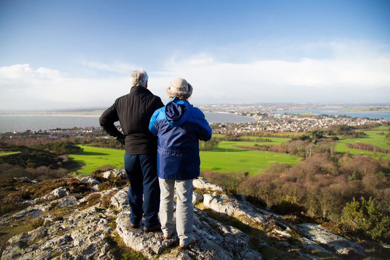 A middle-aged couple standing on top of a hill looking out over a beautiful Irish landscape.
