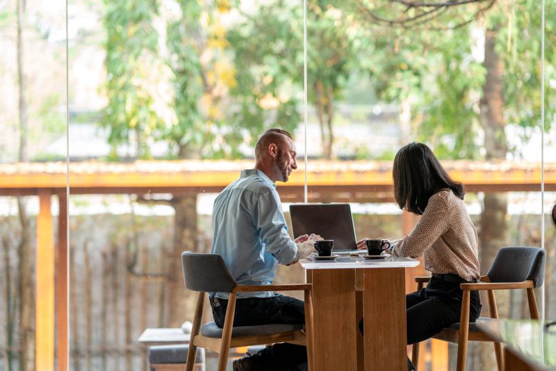 A financial advisor sits across the table from a client in a room with large windows. 