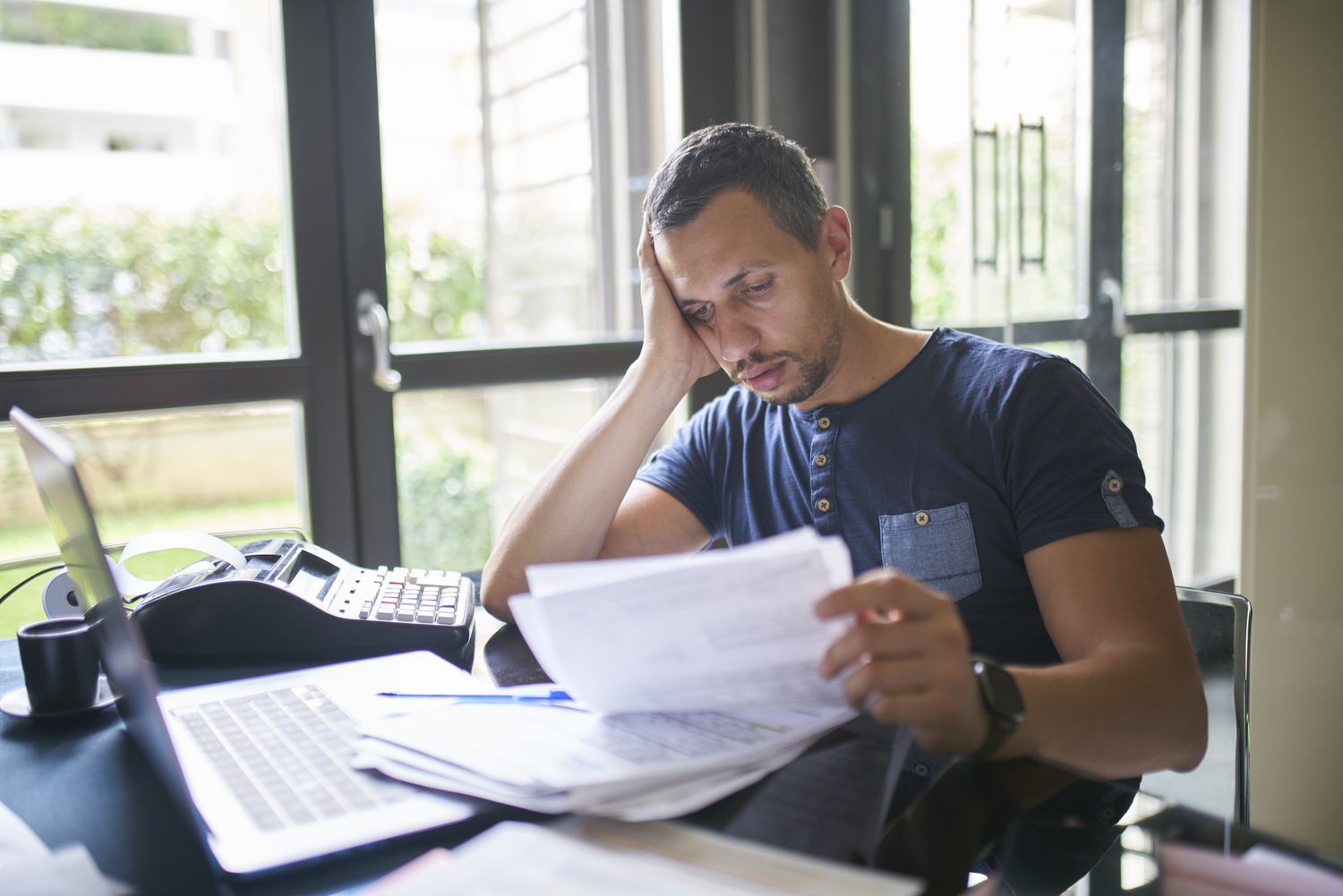 Many sitting at a desk holding his head and studying paperwork.