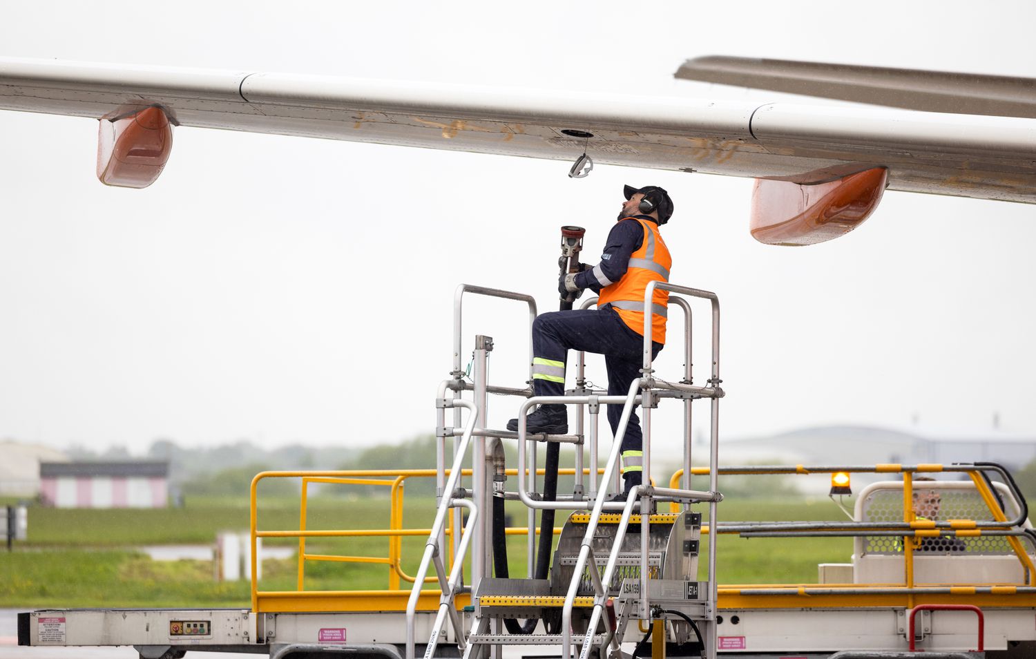 An employee prepares to attach a refueling hose to a passenger aircraft.