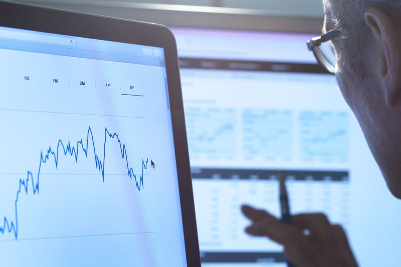man looking at computer screens with line graphs