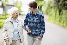 Young woman helping elderly woman walk down street.