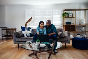 A man and a woman sit on a couch looking at a laptop on the coffee table