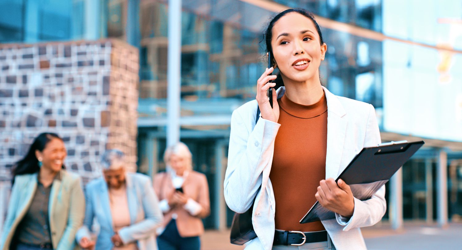  Businesswoman Talking On Phone With Colleagues In Background Outside Office Building