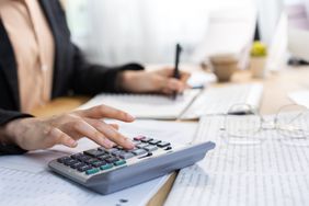 Woman working at a desk writing on a notepad and using a calculator.