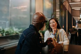 A man and woman look engaged in conversation as they have a casual meal in a cafe in the evening. 