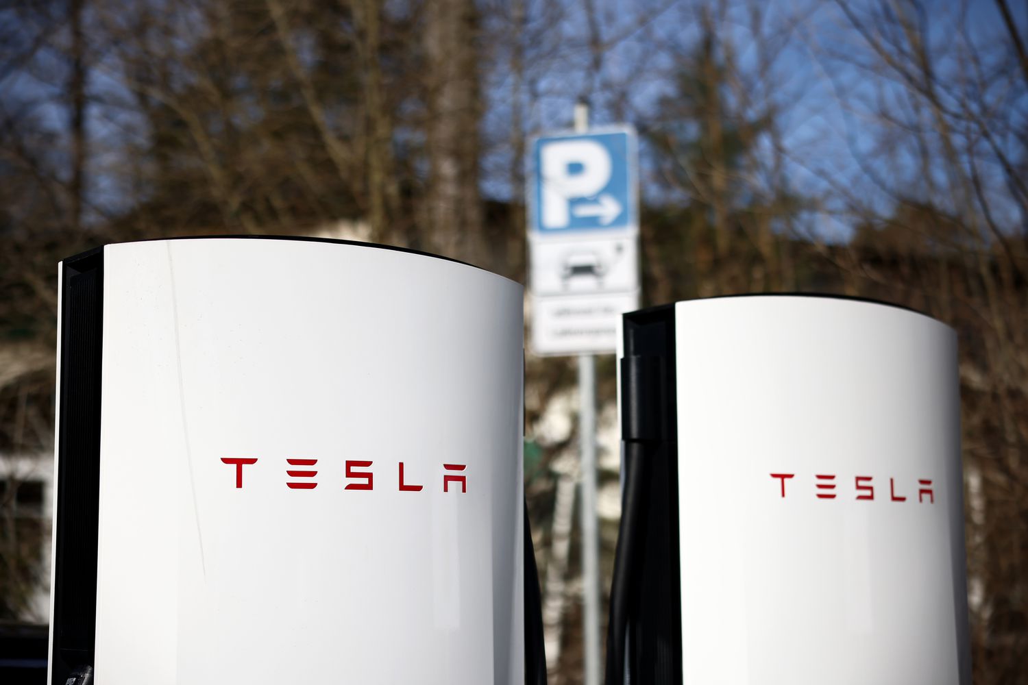 The red Tesla logo is seen on a pair of white Tesla charging stations.