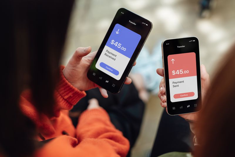 Two friends hold cellphones and transfer money through a mobile app to each other.