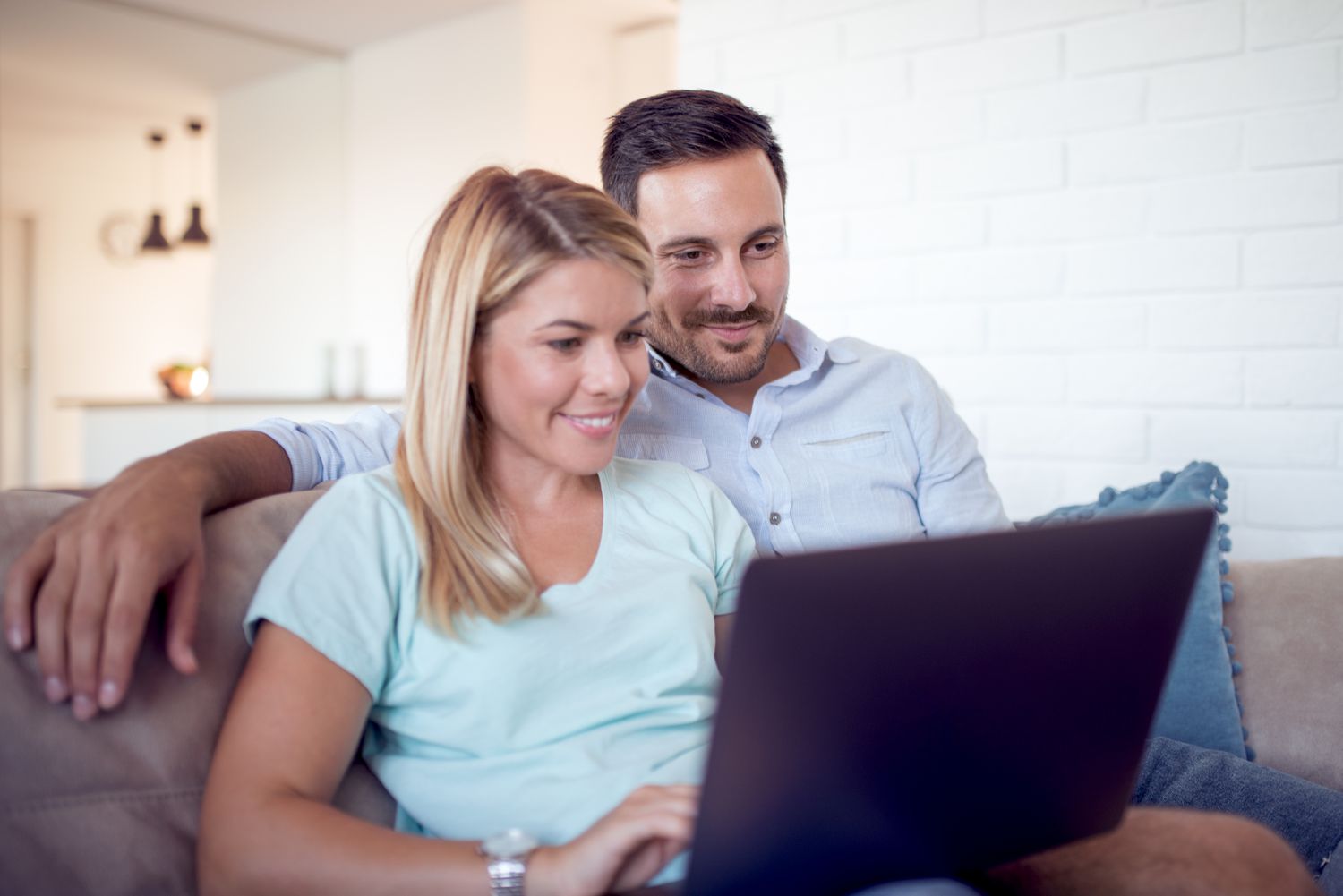 Couple in their 30s sitting on their sofa and looking at mortgage rates on a laptop