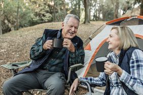 Happy senior having coffee on a camping trip in front of their tent.