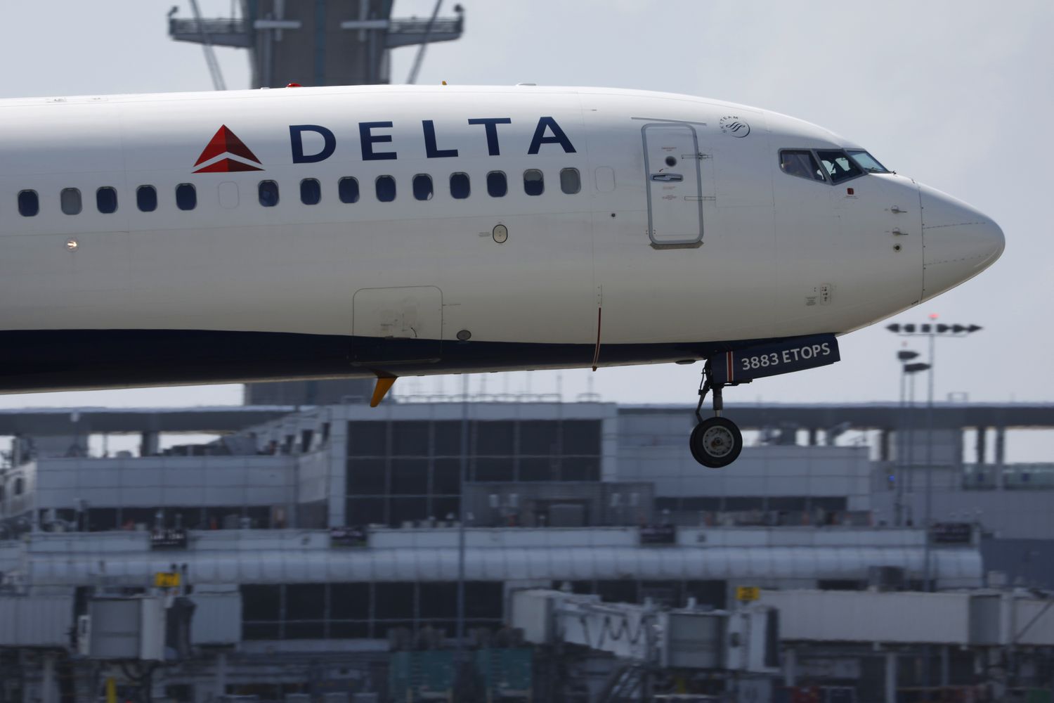 A Delta plane lands with an airport building in the background.