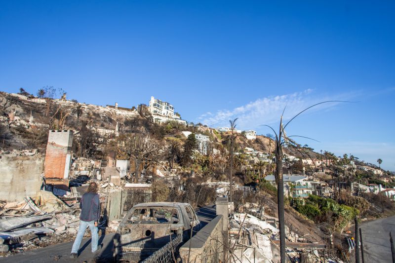 A man walks down the street past burned cars and homes due to the wildfires in Southern California