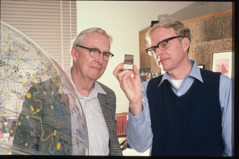 Researchers Luis and Walter Alvarez hold up and view a sample of an iridium layer deposit
