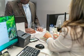 Cropped shot of a female bank teller counting US currency for an unidentifiable black male customer.