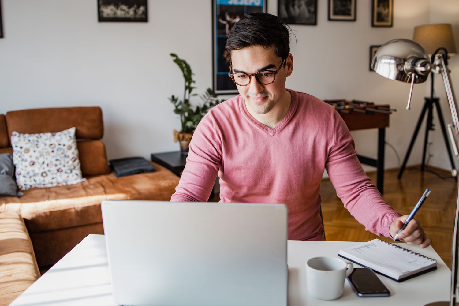 A young man sits at a table with a laptop and a notepad.