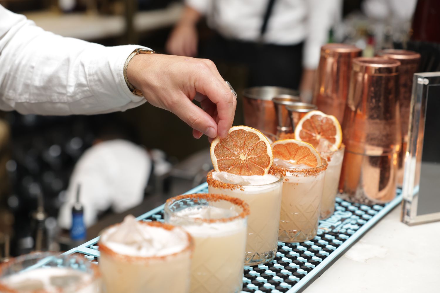 A bartender garnishes a line of cocktails on a bar
