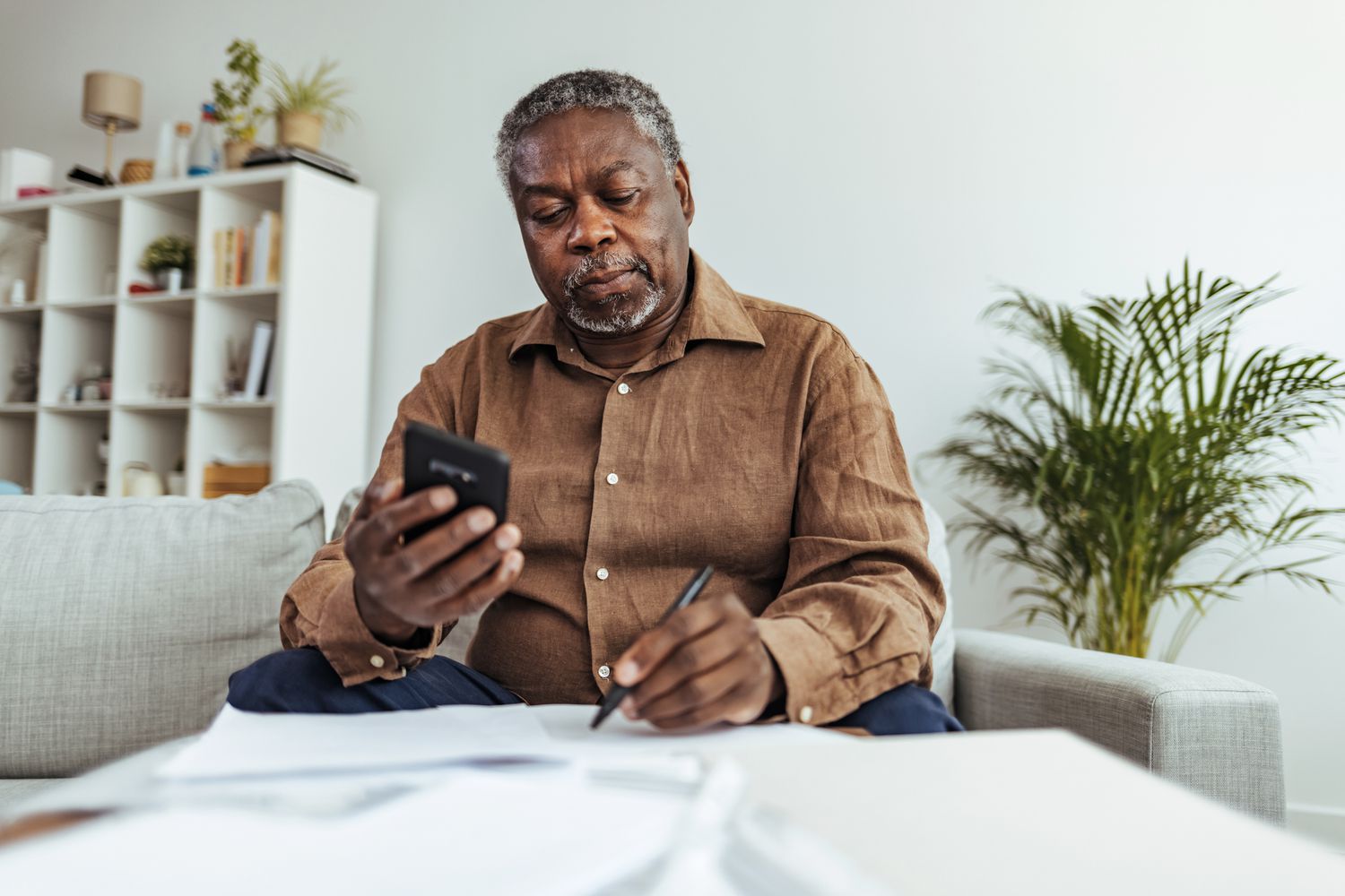 Senior Adult Man With Stacks of Papers and Envelopes holding a smartphone