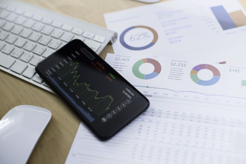 Smartphone on a table showing financial data with papers on the table showing pie charts