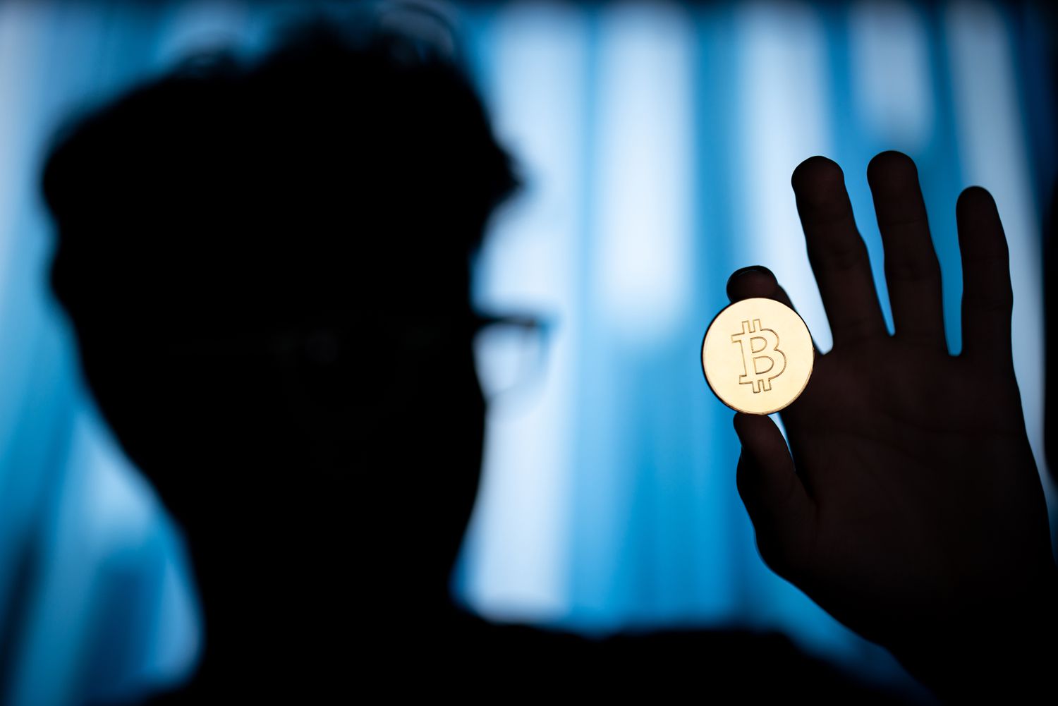 A silhouetted person holds up a bitcoin.