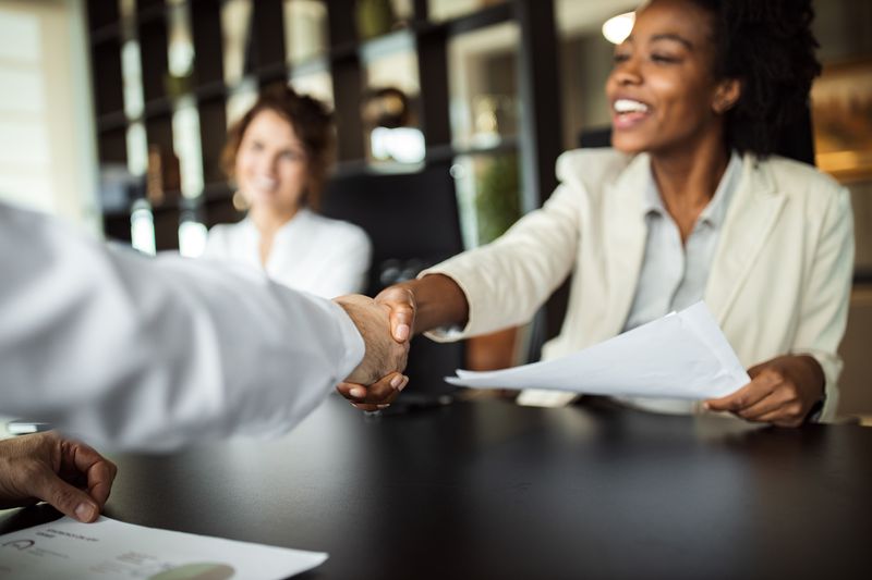 Businesswoman shaking hands with someone across a table.