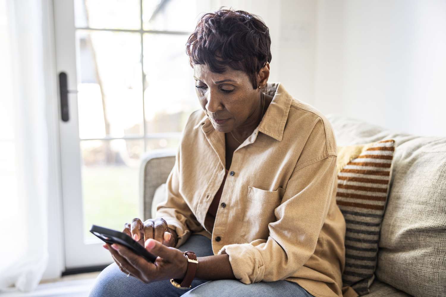 Woman sitting on a couch in a well-lit home using her cell phone.