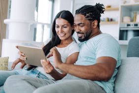 Young couple sitting on their sofa and looking happily at mortgage rates on a tablet