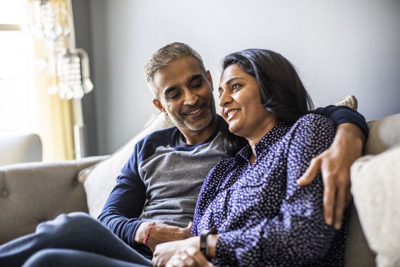 a man and woman sit on a couch at home talking