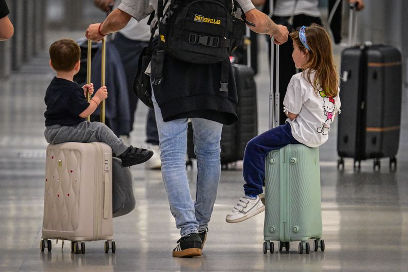 A person rolls two suitcases with children seated on them.