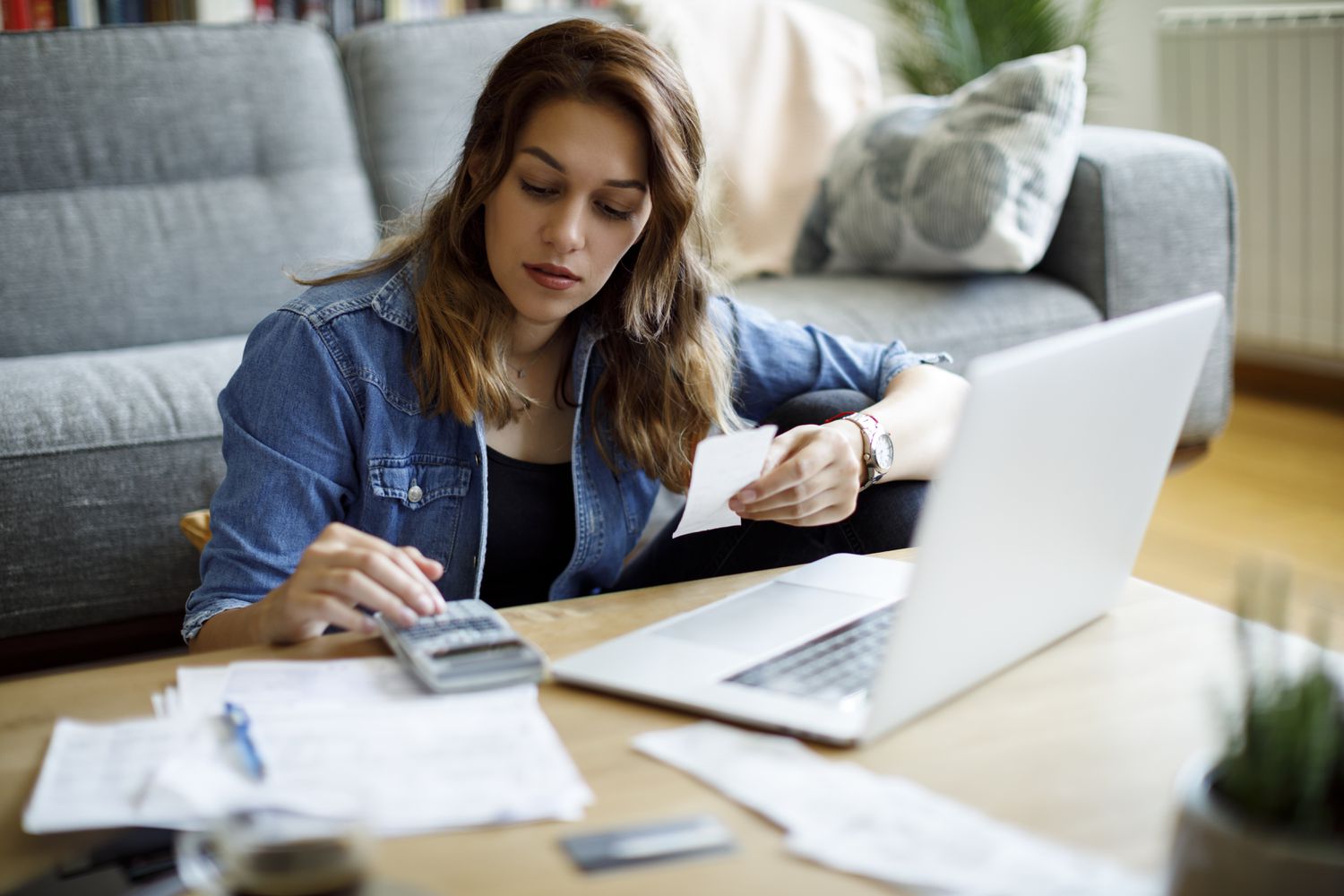 Woman sitting on the floor using computer and calculator at coffee table