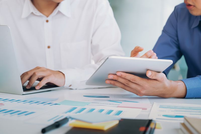 midsection of businessmen working on laptops with graphs and charts on the table around them