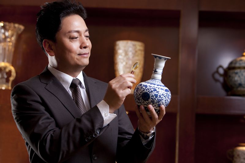 Man in a suit looks at antique vase through a magnifying glass