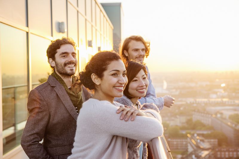 Four people in their 20s watching sunset from an urban balcony