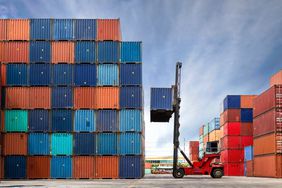 Crane lifting up container in yard full of containers. 