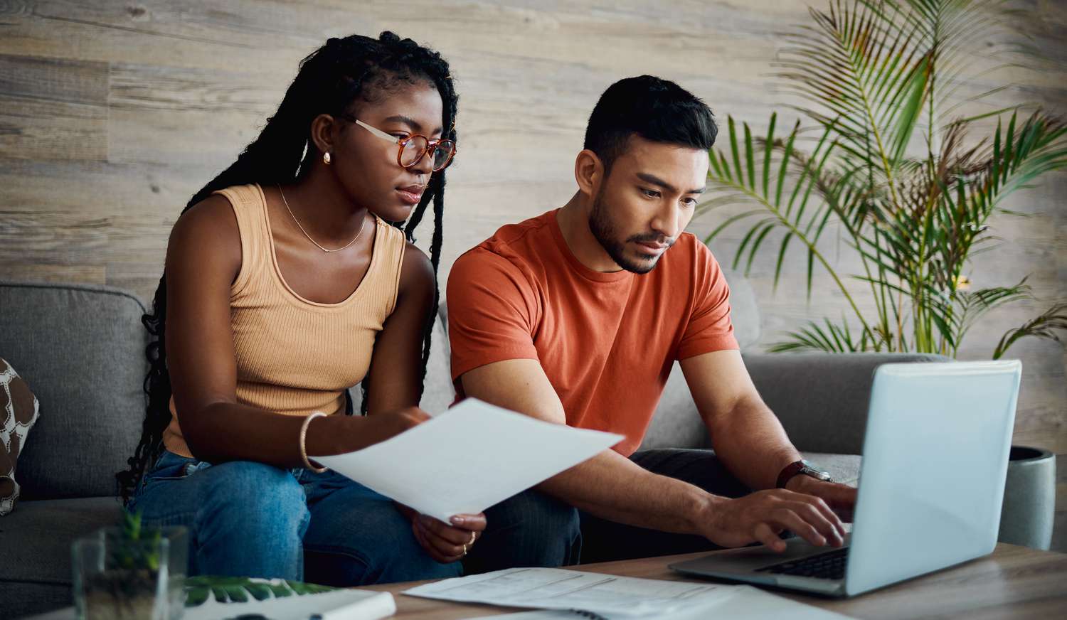 Young couple sitting on their sofa and looking a documents and a laptop