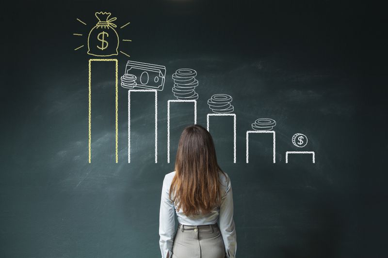 A woman staring at a blackboard chart for money