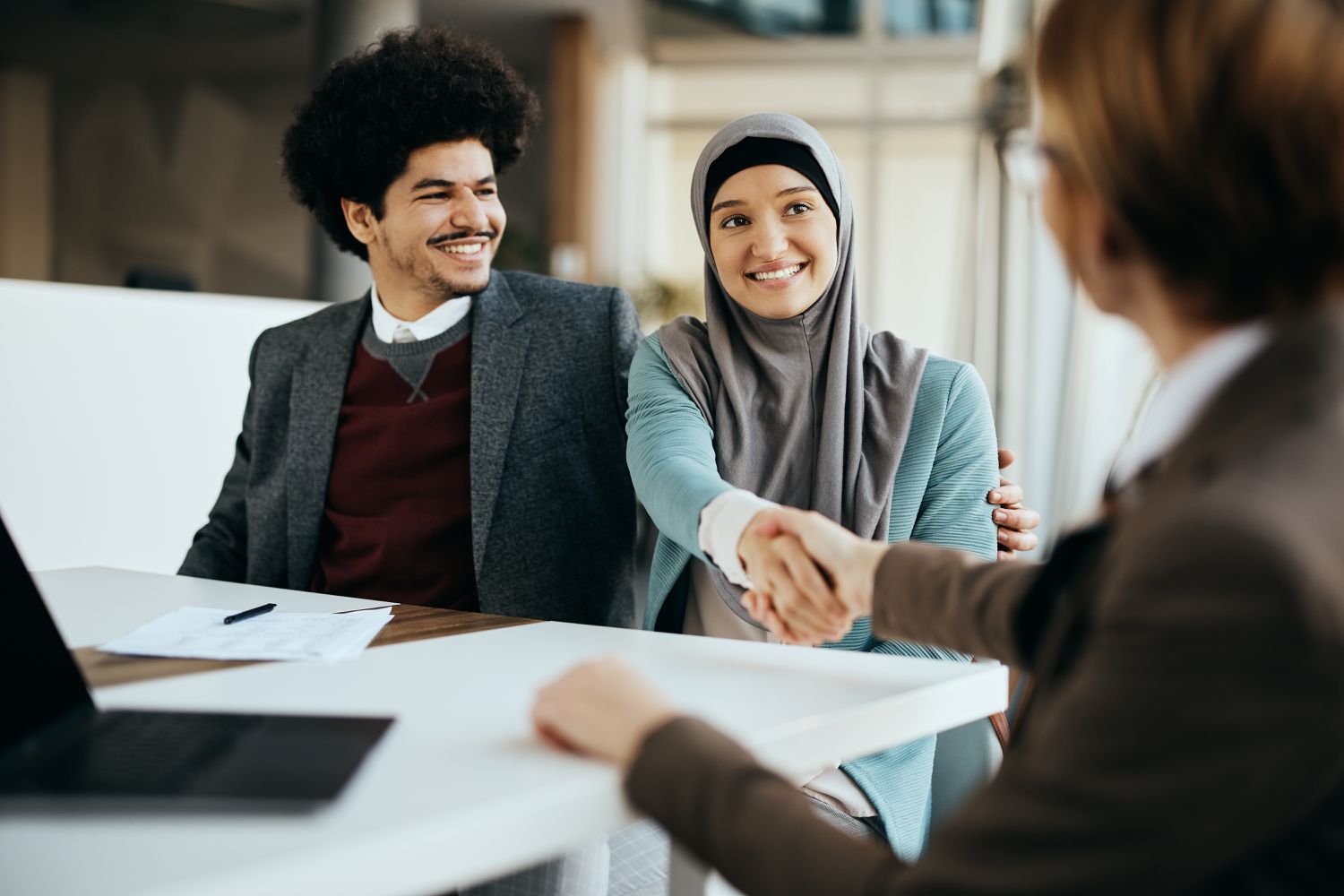 A young couple smile as they shake hands with a bank loan officer after finding out that they are approved for a loan. 