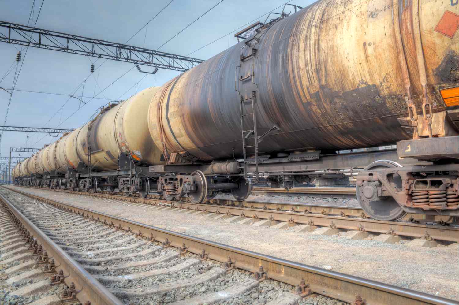 Railcars carry a line of oil tankers streaked with oil from frequent as they move slowly along a sidetrack into a railyard.