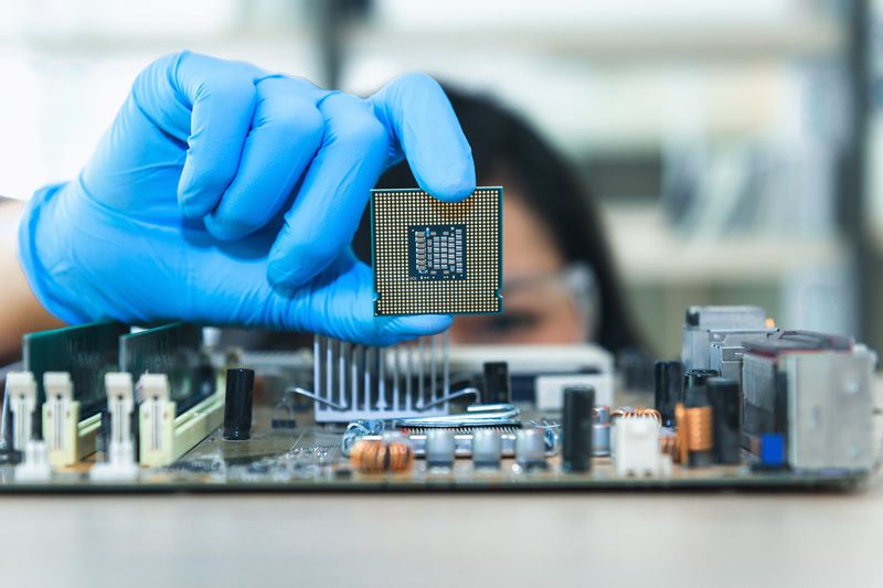Engineer holds computer chip next to circuit board.